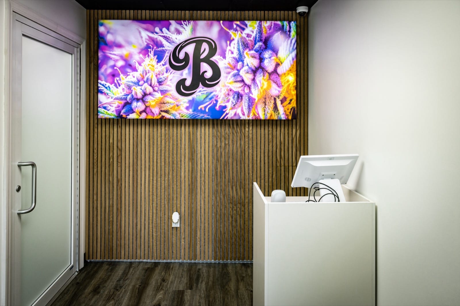 Backlit Beleaf B logo sign over cannabis flower artwork at Beleaf Calverton dispensary